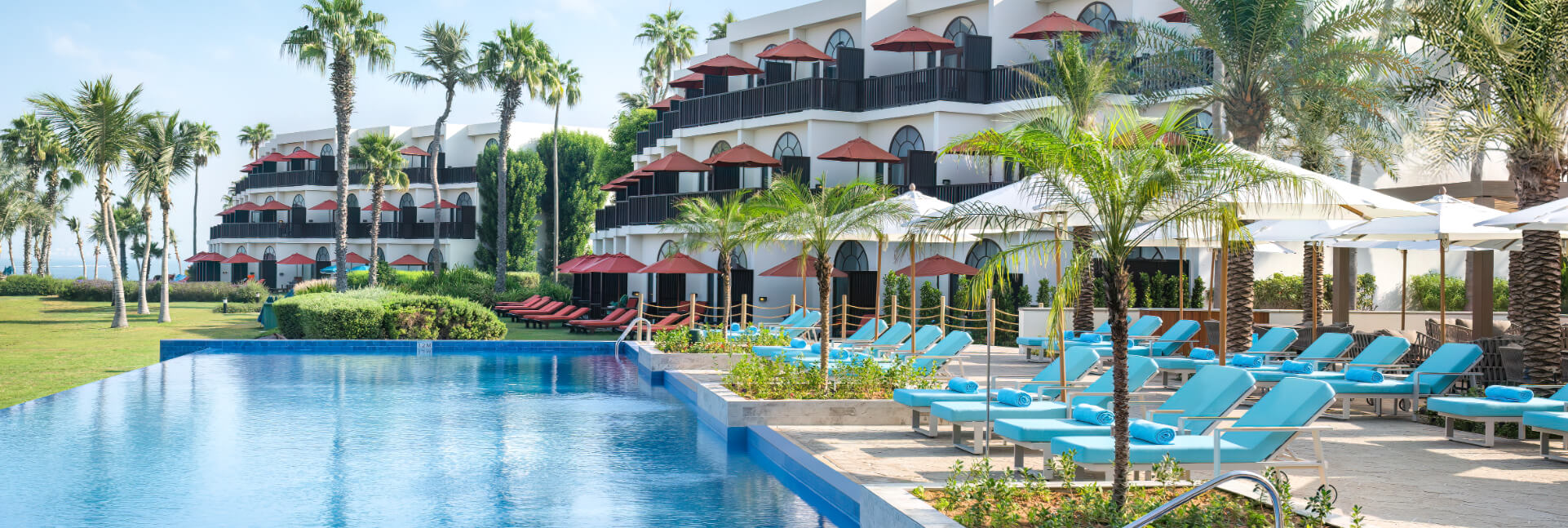 An infinity pool lined with light blue loungers and white umbrellas at a tiered JA Resorts & Hotel with palm trees