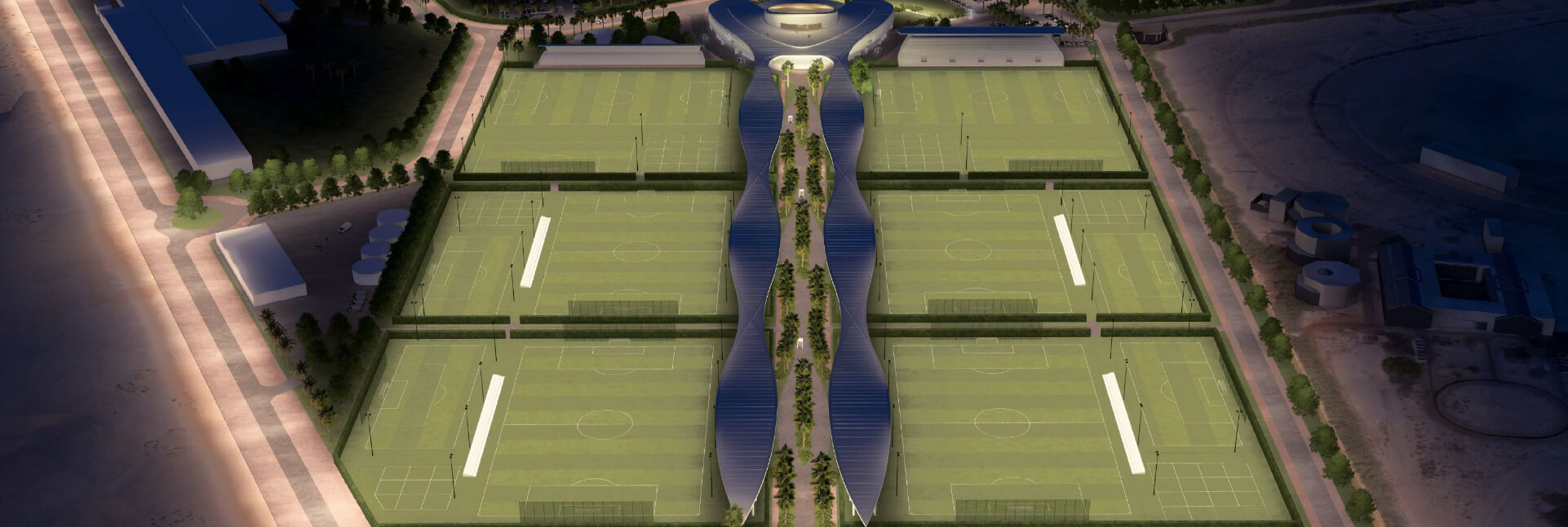 Aerial night view of an illuminated sports complex with multiple green pitches and modern architecture